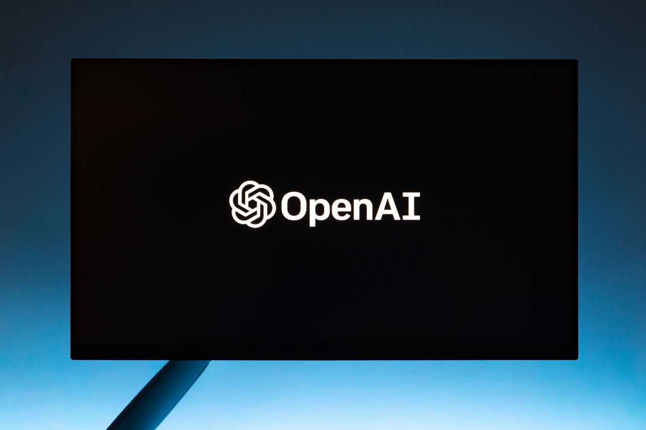Minimalist display of OpenAI logo on a screen, set against a gradient blue background.